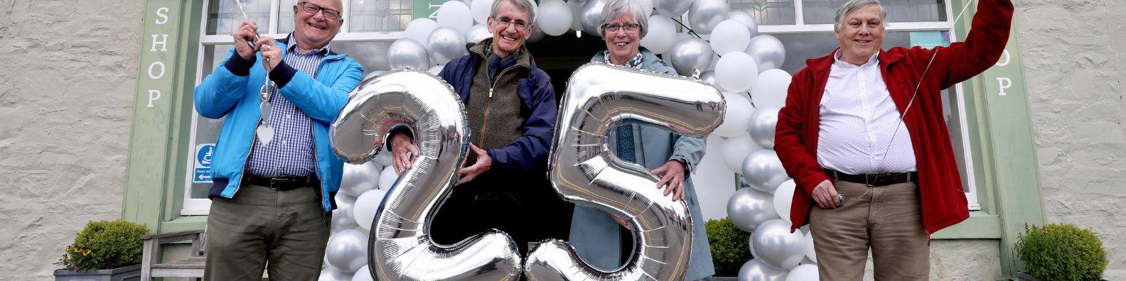 Four people standing in front of  Mercat Cross, Wigtown, holding silver balloons for the twenty fifth anniversary of Wigtown's Book Festival.
