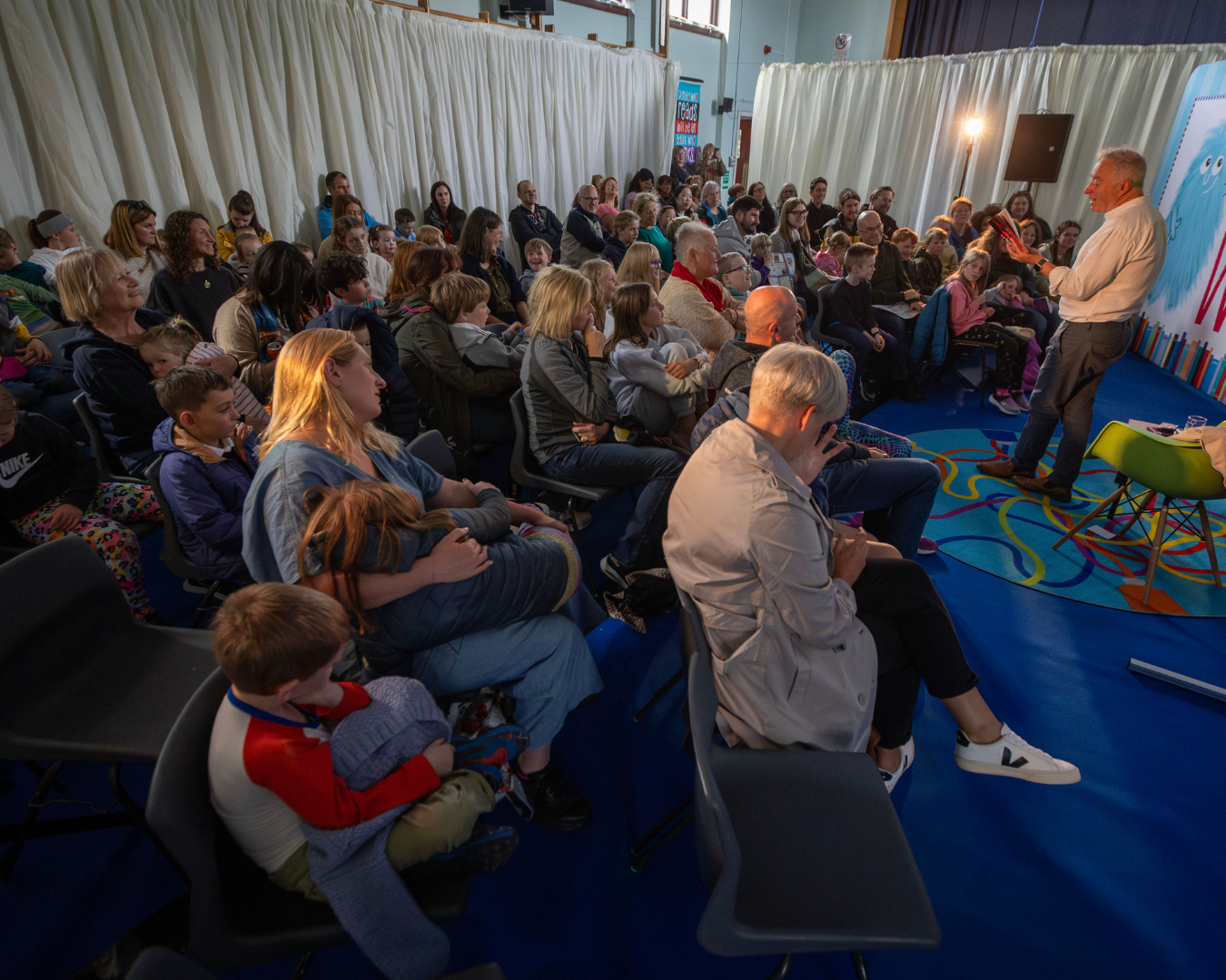 Children's Laureate Frank Cottrell Boyce speaking in front of a large audience of children and families at Big Wig Children's Book Festival