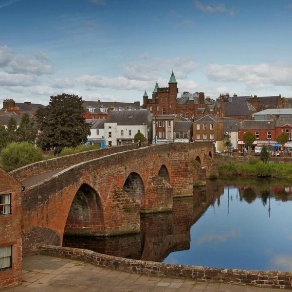 A bridge over the river Nith in Dumfries. Buildings and a church spire in the background.