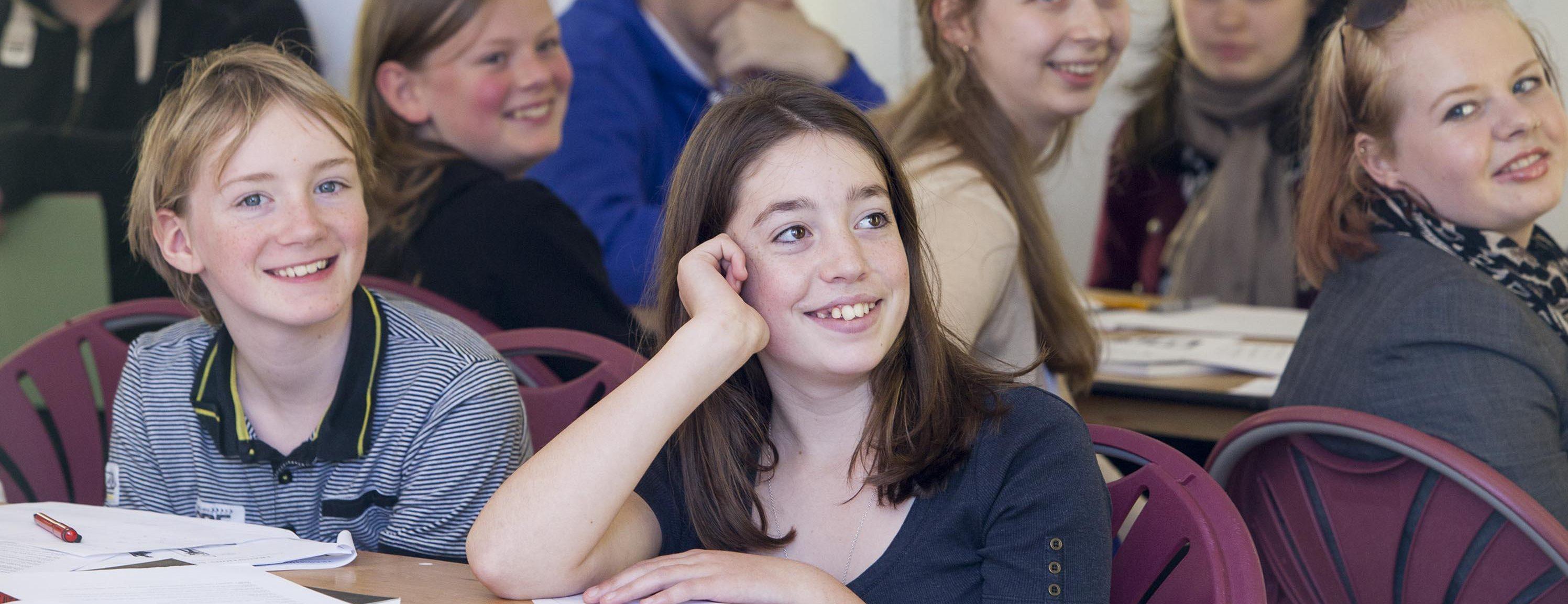 A group of young adults sitting at tables animatedly listening at a Wigtown Book Festival event. Books, papers and pencils are in front of them.