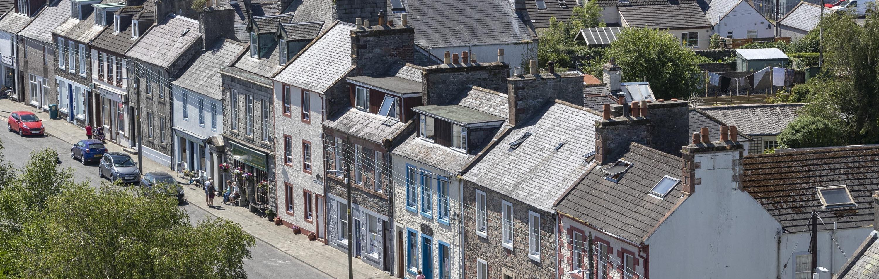 A view from the air of North Main Street, Wigtown, Scotland's National Book Town. Terraced houses and shops in various colours, trees in the forefront.