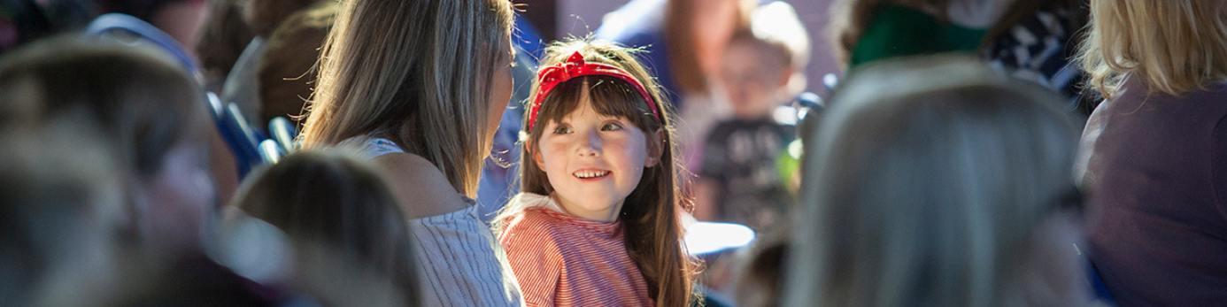 A young child is highlighted by a ray of sunshine in a crowd at a Wigtown Book Festival event.