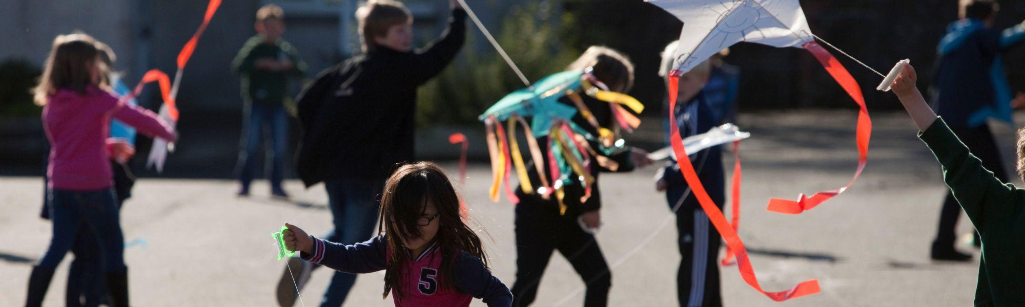 Children running around a playground holding kites they made at a Children's Book Festival event.