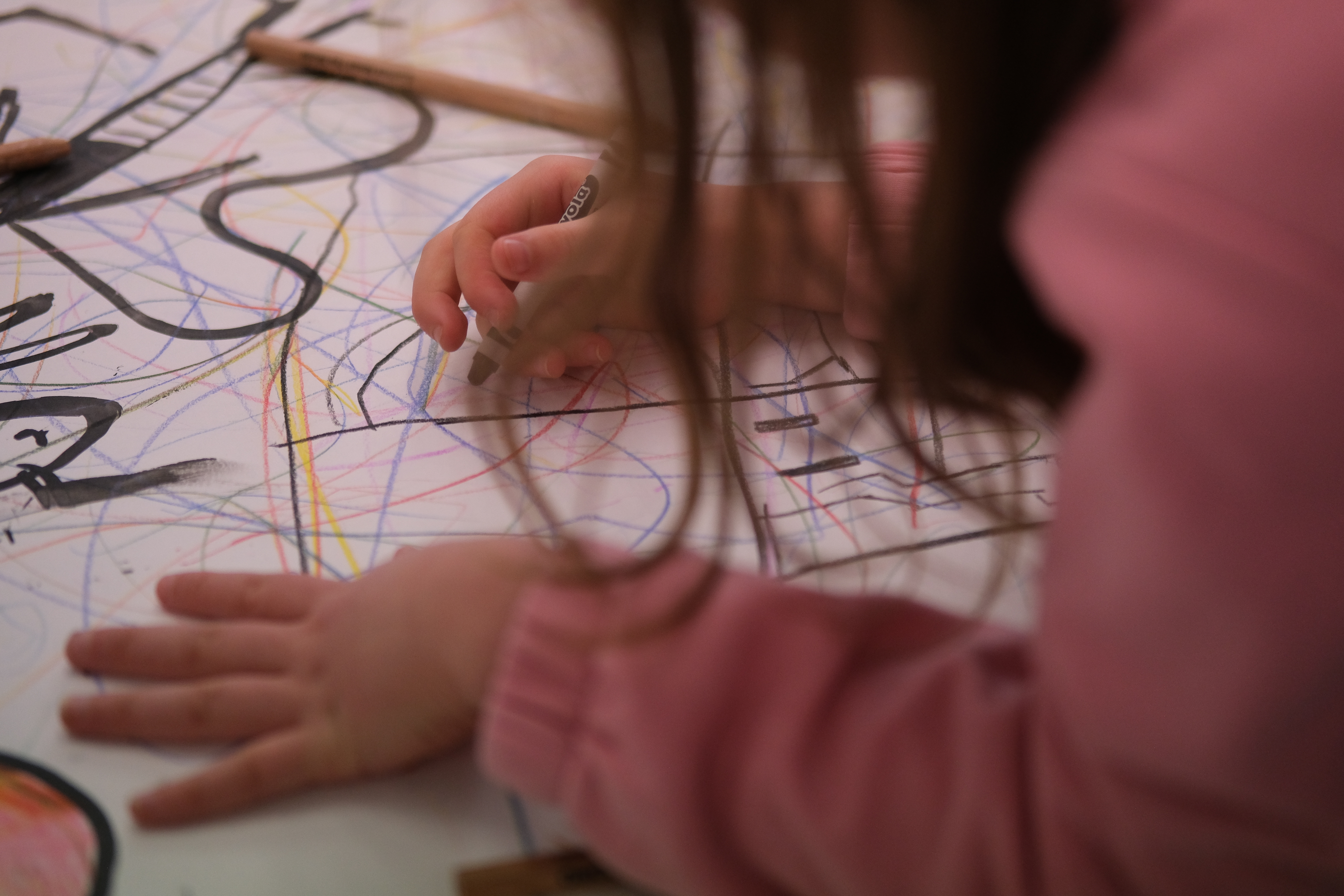 A child is sitting drawing at a desk with black crayons for a Children's Book Festival event.