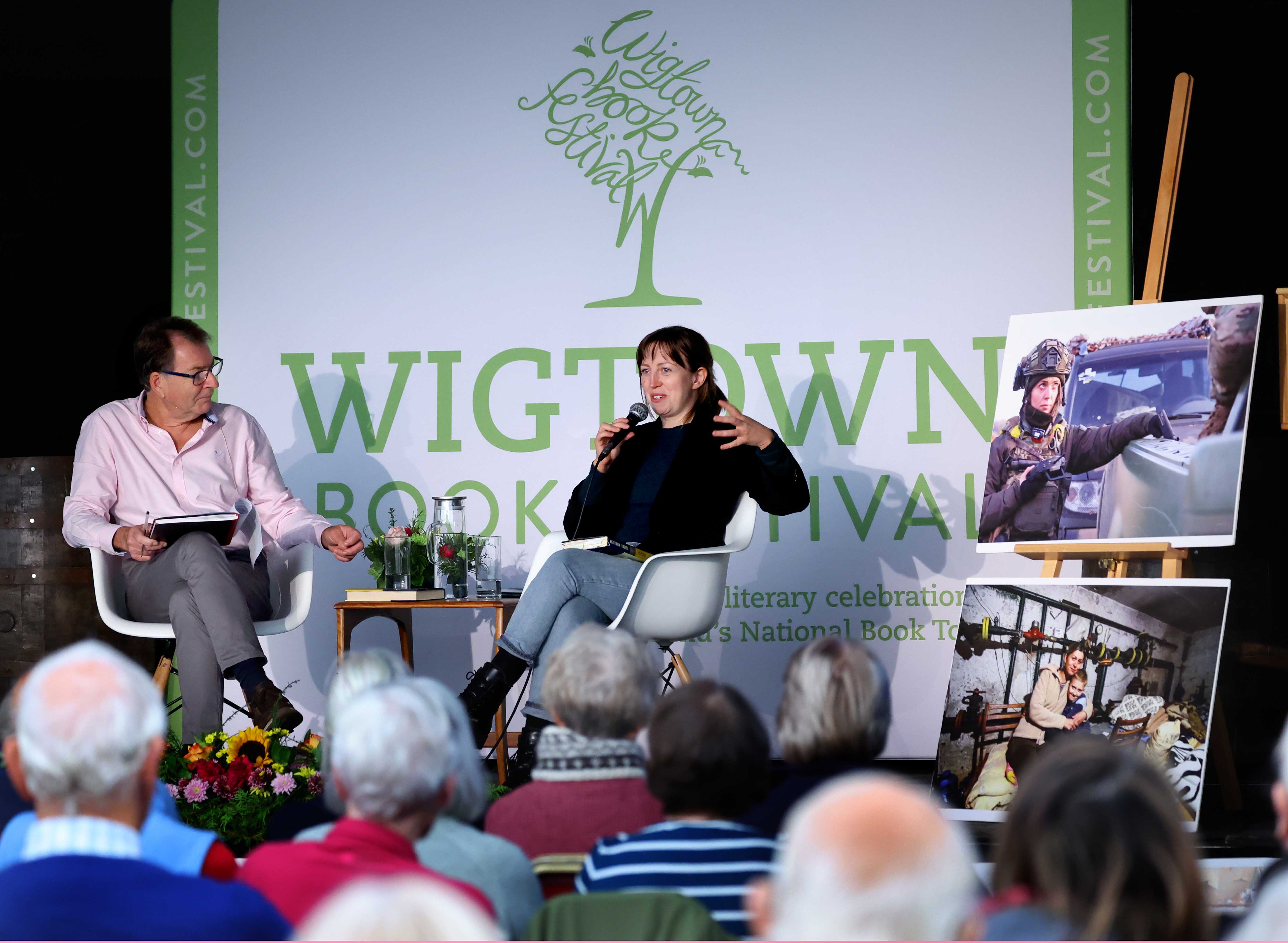 Jen Stout at her event, on stage in front of a Wigtown Book Festival banner, speaking to the audience.