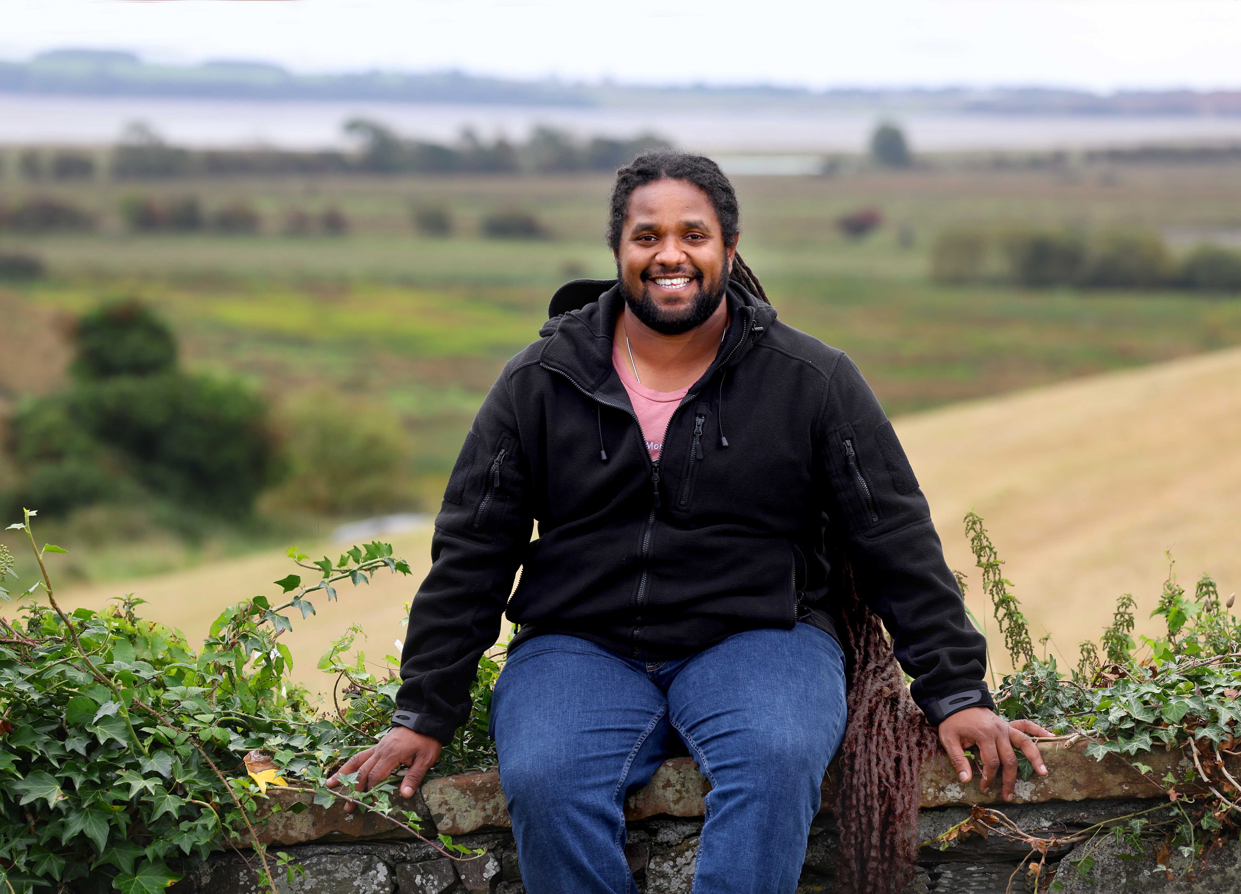 Hamza Yassin seated on a wall with Wigtown Bay in the background.