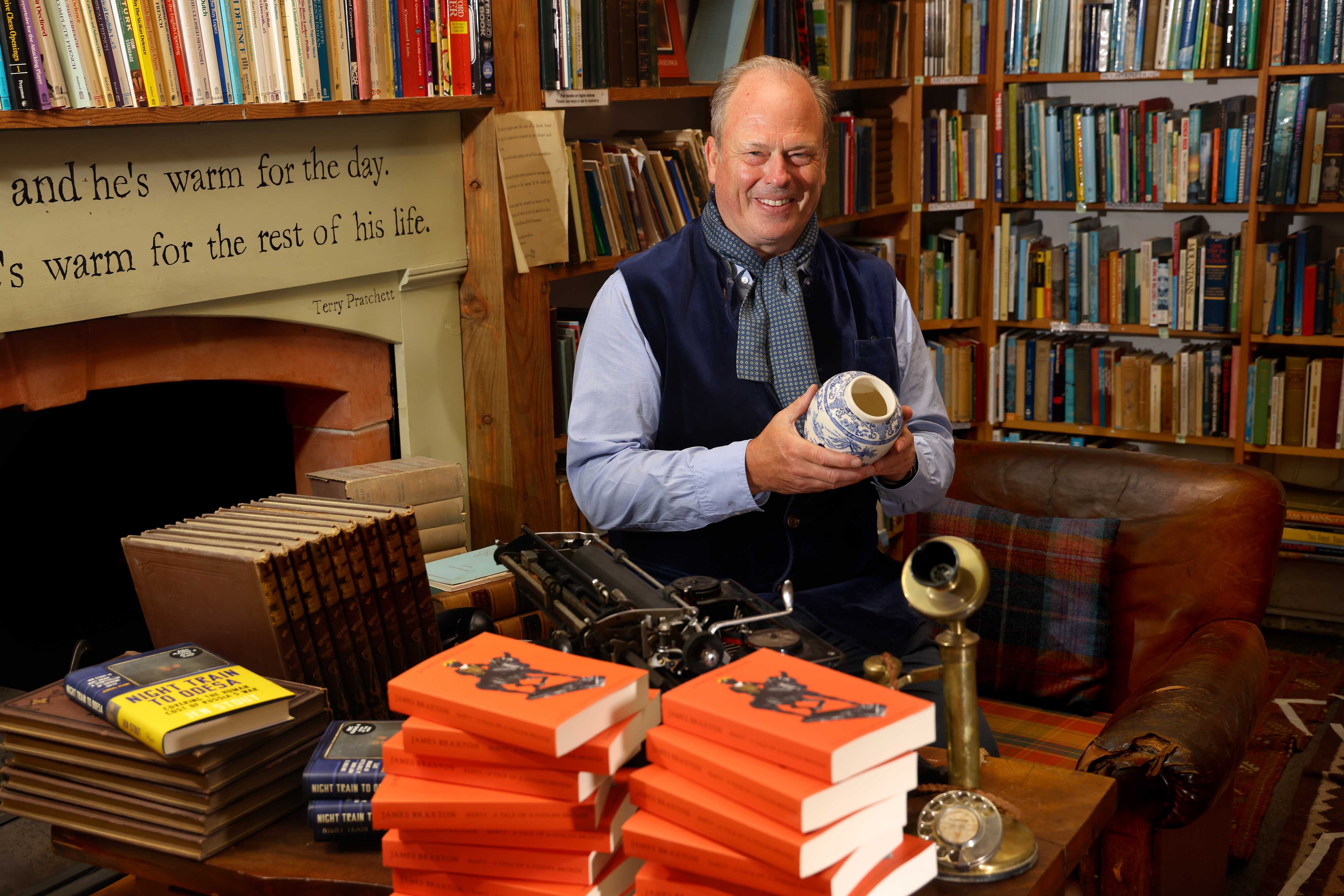 James Braxton in a bookshop, holding up a blue and white antique vase, mid shot