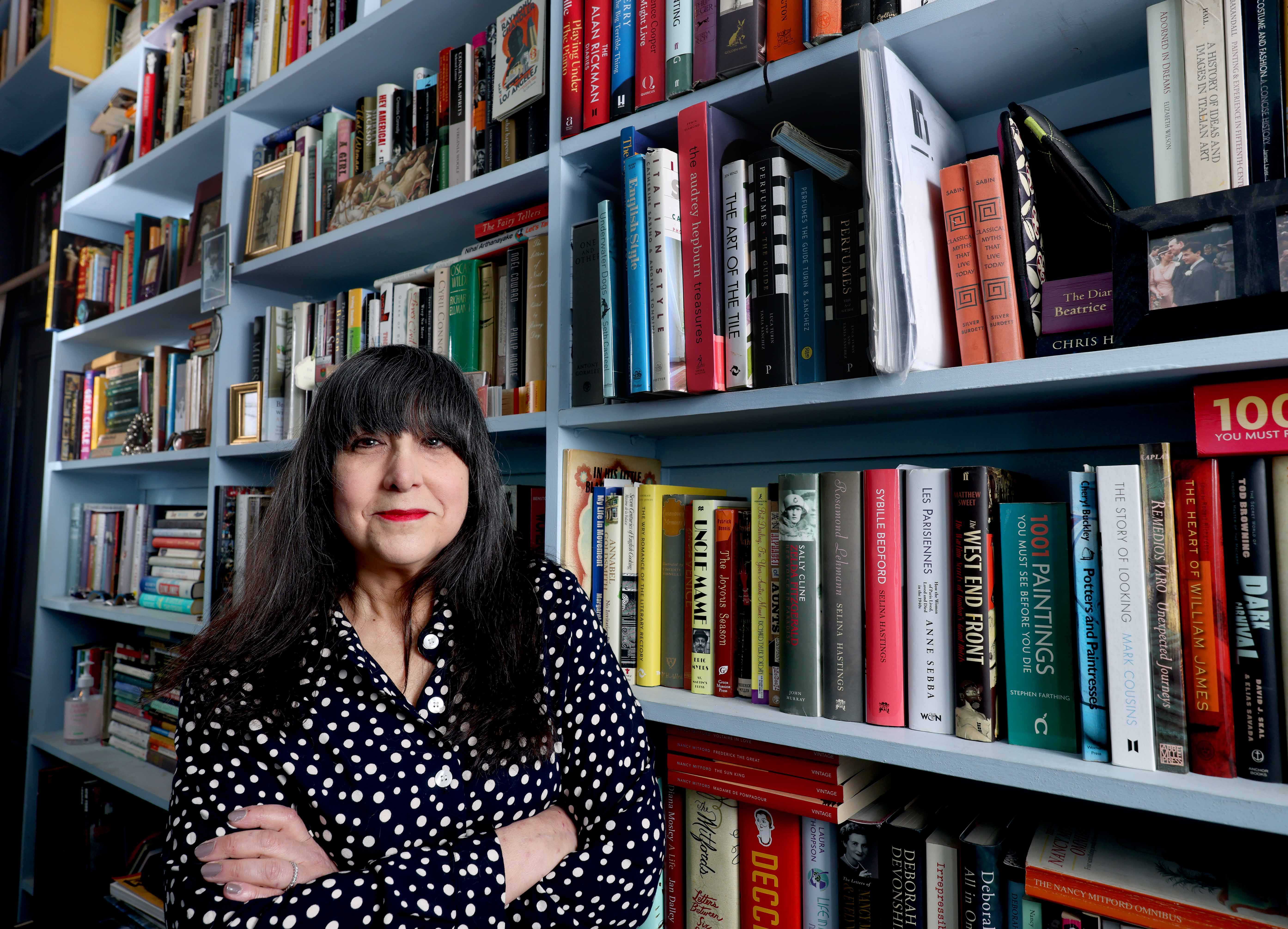 Lee Randall standing in a bookshop with her arms folded in front of her. The bookshelves behind her are full of books.