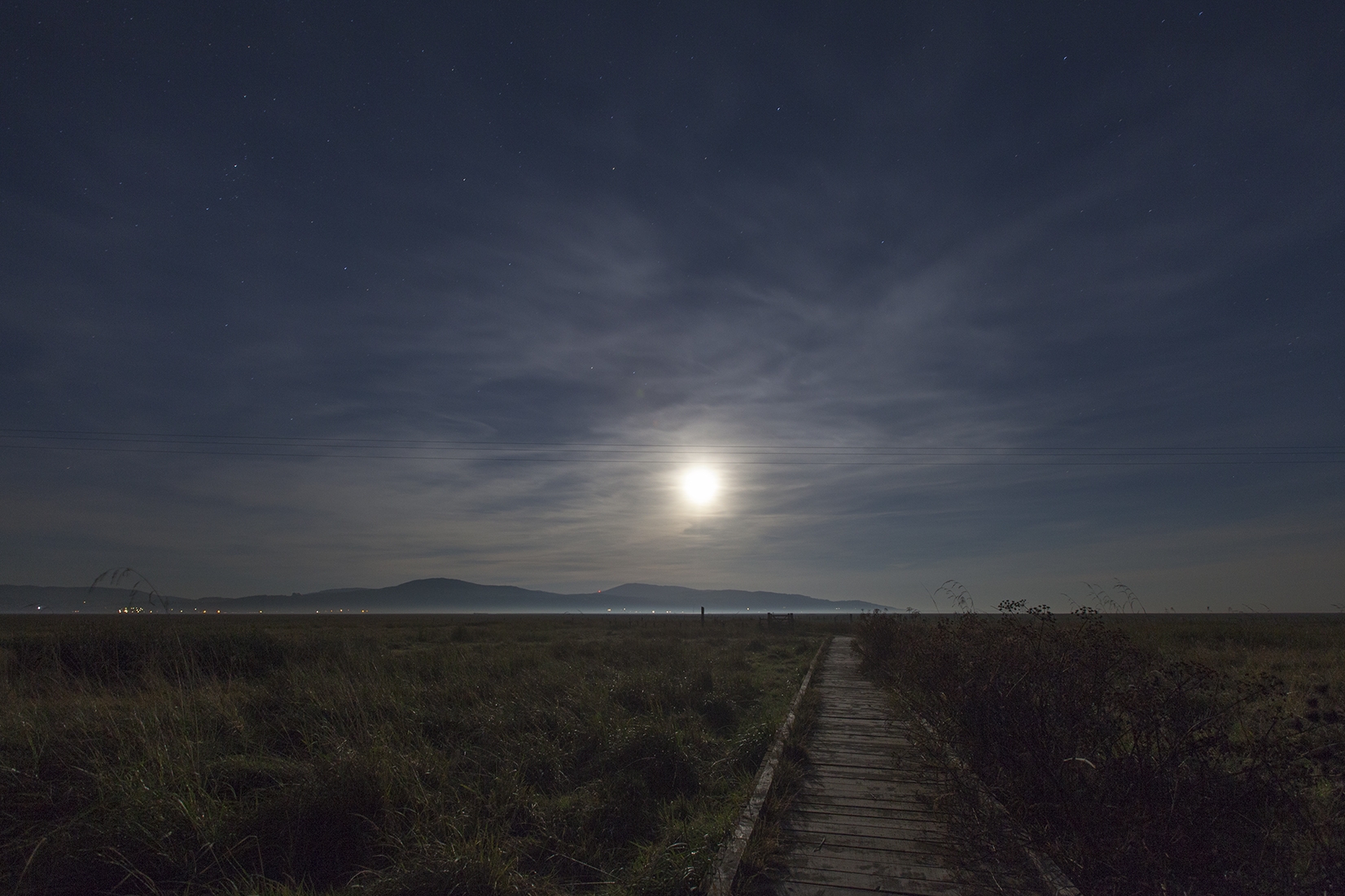 The salt marshes and the wooden walkway to The Martyrs Stake lit up by the moon under a dark sky.