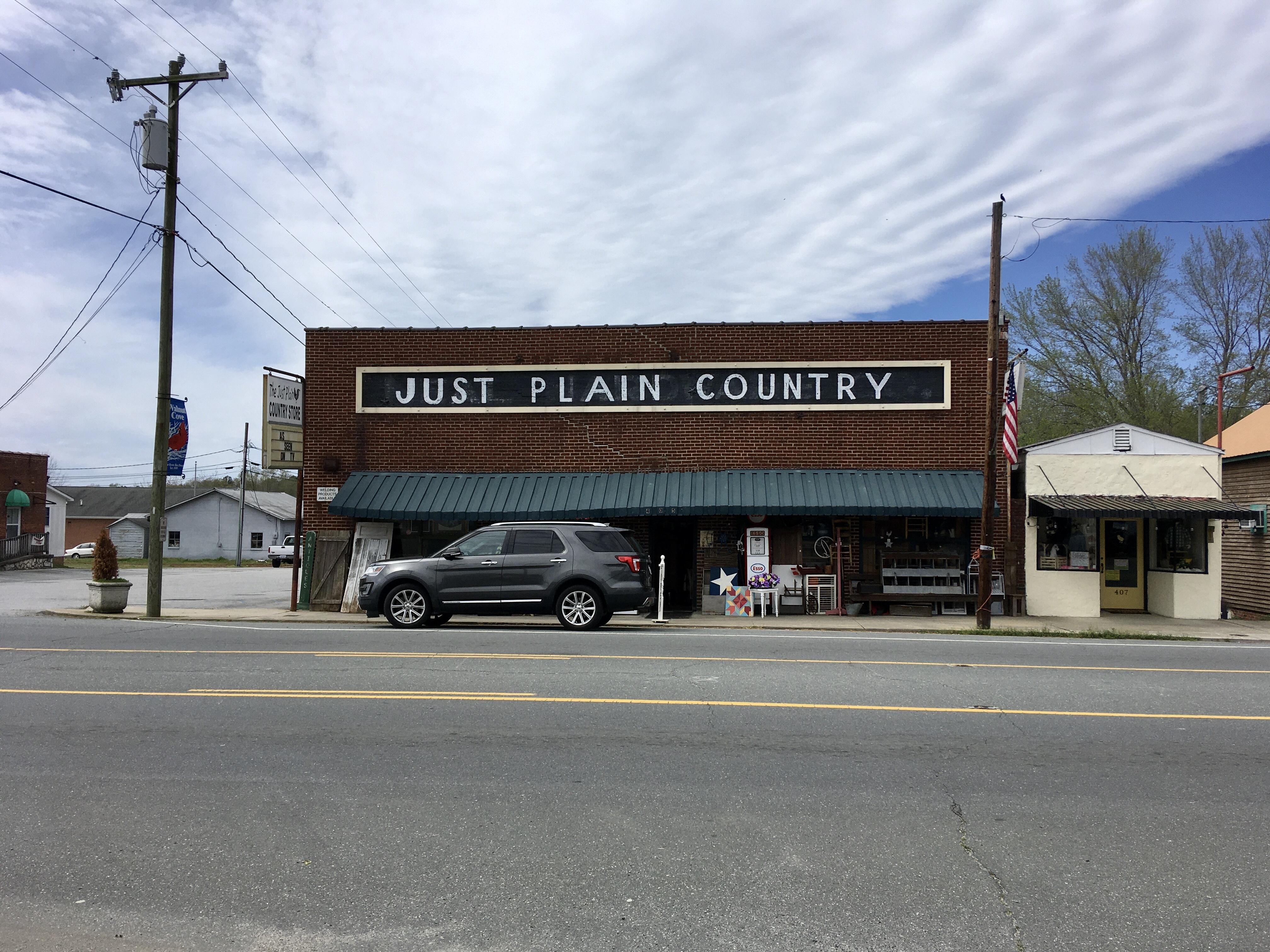 A red brick country store called 'Just Plain Country' in North Carolina. A car sits outside, telegraph poles either side.