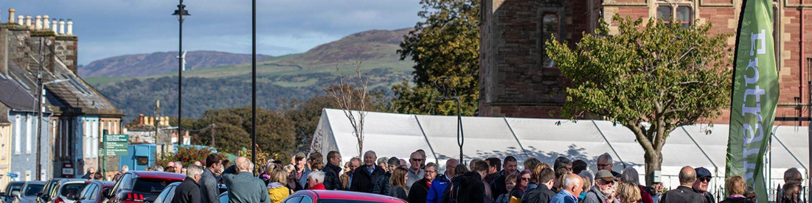 At Wigtown Book Festival crowds are queuing outside a marquee for an event. Views to the hills beyond on a sunny autumn day.