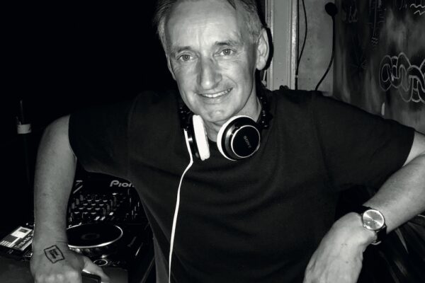 Pat Nevin is standing at a DJ booth wearing headphones.
