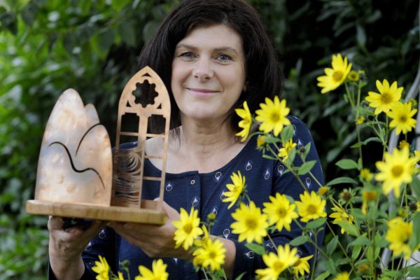 Dani Garavelli is standing in a garden with yellow flowers holding the Anne Brown Essay Prize trophy.