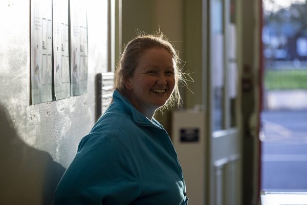 Anne Barclay, Operational Director of Wigtown Festival Company is standing smiling, her back to a wall in Wigtown County Buildings.