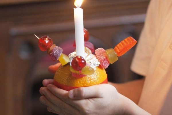 A child holding an orange adorned with sweets and a candle for Christingle.