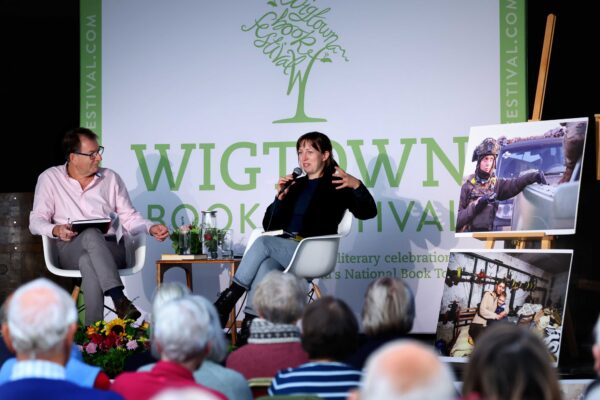 Jen Stout at her event, on stage in front of a Wigtown Book Festival banner, speaking to the audience.