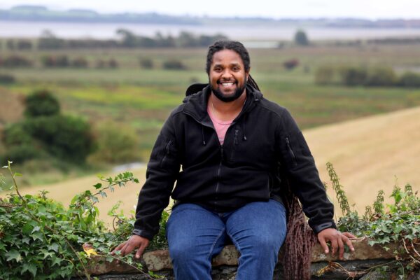 Hamza Yassin seated on a wall with Wigtown Bay in the background.