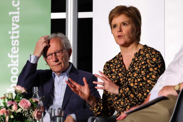 Henry McLeish and Nicola Sturgeon seated on stage at Wigtown Book Festival. McLeish scratches his head, Sturgeon gestures with her hands while speaking.