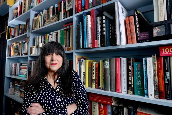 Lee Randall standing in a bookshop with her arms folded in front of her. The bookshelves behind her are full of books.