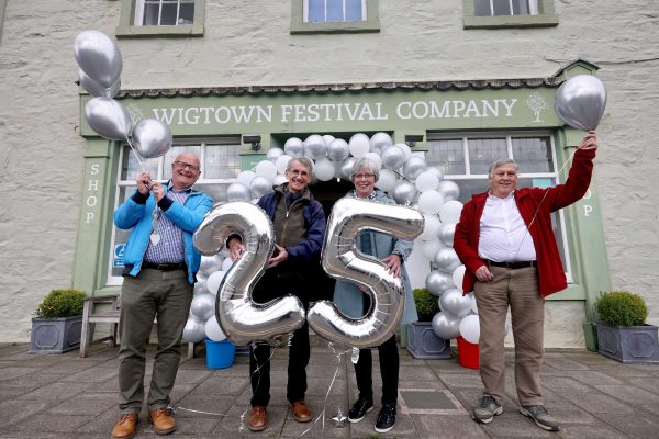 Four people standing outside Wigtown Festival Company bookshop holding silver balloons to celebrate the twenty fifth anniversary of Wigtown Book Festival.