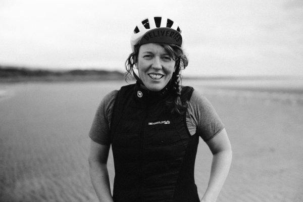 Jenny Graham standing on a beach at low tide wearing a bike helmet.