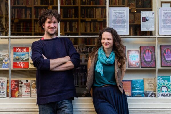 Ben Please and Beth Porter of the Bookshop Band stand outside a bookshop.