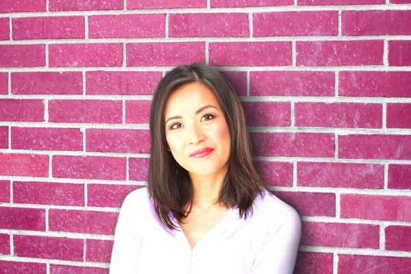 Head shot of Sue Cheung standing against a red brick wall.