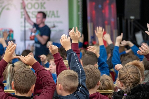 School children raising their hands and engaging with an author at a Children's Book Festival event in Wigtown, Scotland's National Book Town.