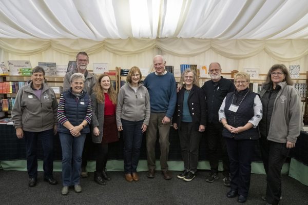 A group of Wigtown Book Festival volunteers standing smiling in the marquee against a backdrop of books on display.