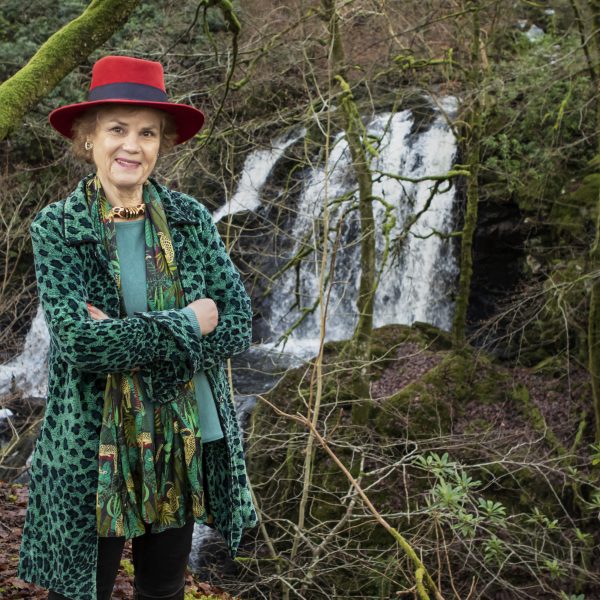 Cathy Agnew, Chair of Wigtown Festival Company standing in front of a waterfall in a forest.