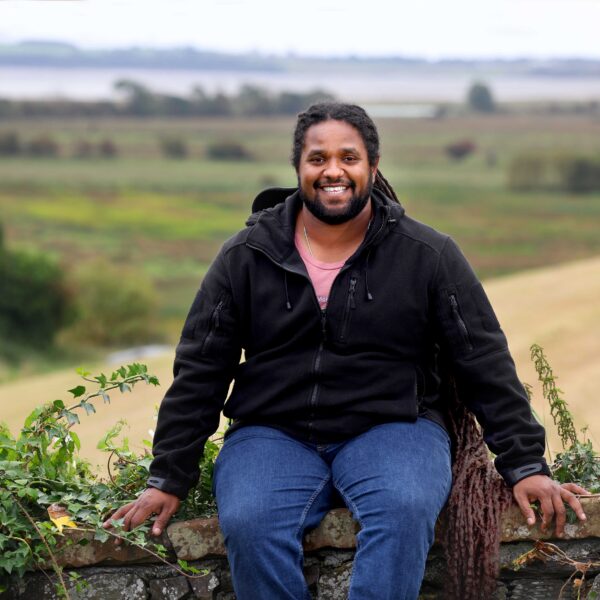 Hamza Yassin seated on a wall with Wigtown Bay in the background.