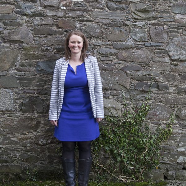 Anne Barclay, Operational Director of Wigtown Festival Company standing in front of a stone wall.