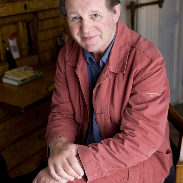 Author Michael Morpurgo sitting in a chair at his desk. Behind him a standing lamp.