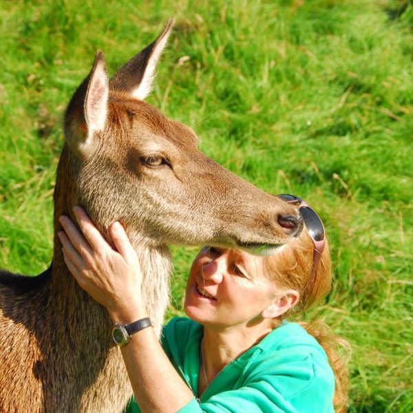 Polly Pullar sits beside a deer, smiling and stroking its neck.