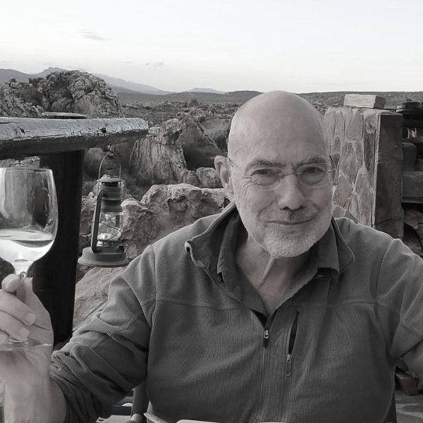 Robin Leiper holding a glass of wine sitting outside with hills in the background.