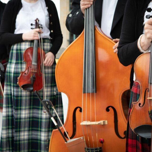 Players from the Scottish fiddle Orchestra stand in formal attire holding their various instruments.