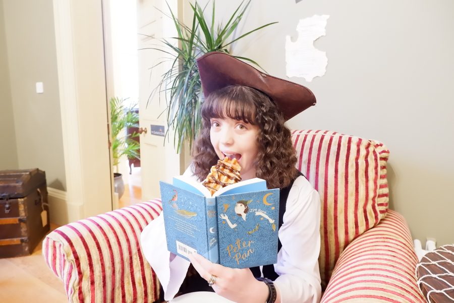 A Young child is dressed in a pirate costume sitting in an armchair reading a book.