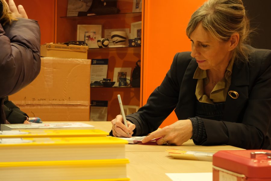 Lauren Child is sitting at a desk signing books at a Big Dog Children's Book Festival.