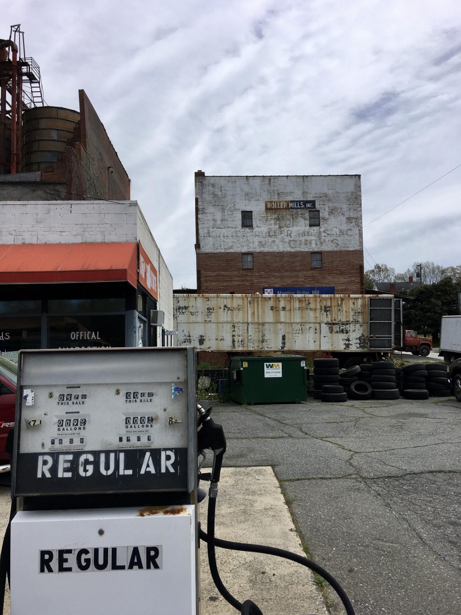A run down petrol station pump in North Carolina. Old buildings in the background.