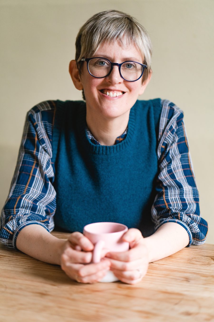 Author Liz Flanagan sitting at a desk smiling with a cup in her hands.