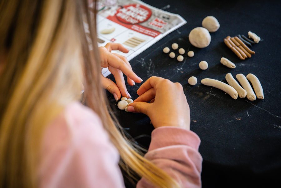 A young child sitting at a table rolling out white modelling clay into balls  to make a sheep, during a Children's Book Festival event.