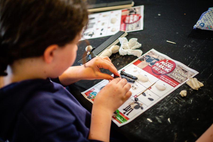 A young child sitting at a table making a model sheep with an instruction leaflet and modelling clay, during a Children's Book Festival event.