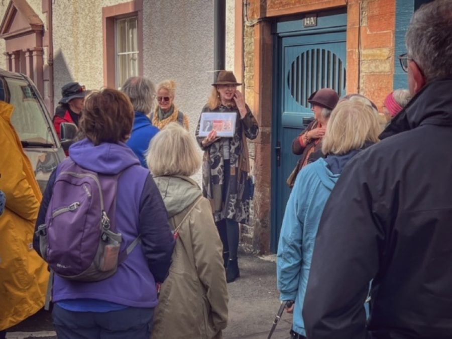 People standing in front of a house in Kirkubright listening to a speaker at a Dorothy L Sayers walk for Wigtown Book Festival