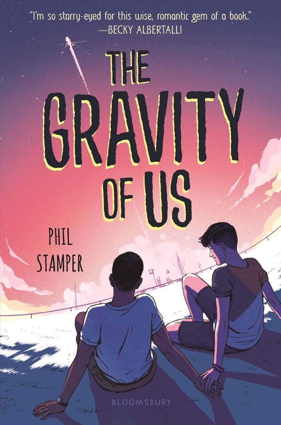 Book cover for 'The Gravity of Us' by Phil Stamper. Two young adults are sitting looking out into the sunset over buildings, their hands are touching. A shooting star races through the sky.