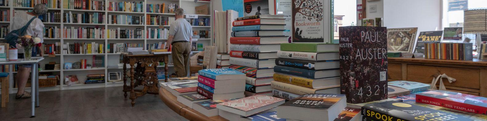 Inside the Wigtown Festival Company Bookshop. Shelves and tables of books with customers browsing.