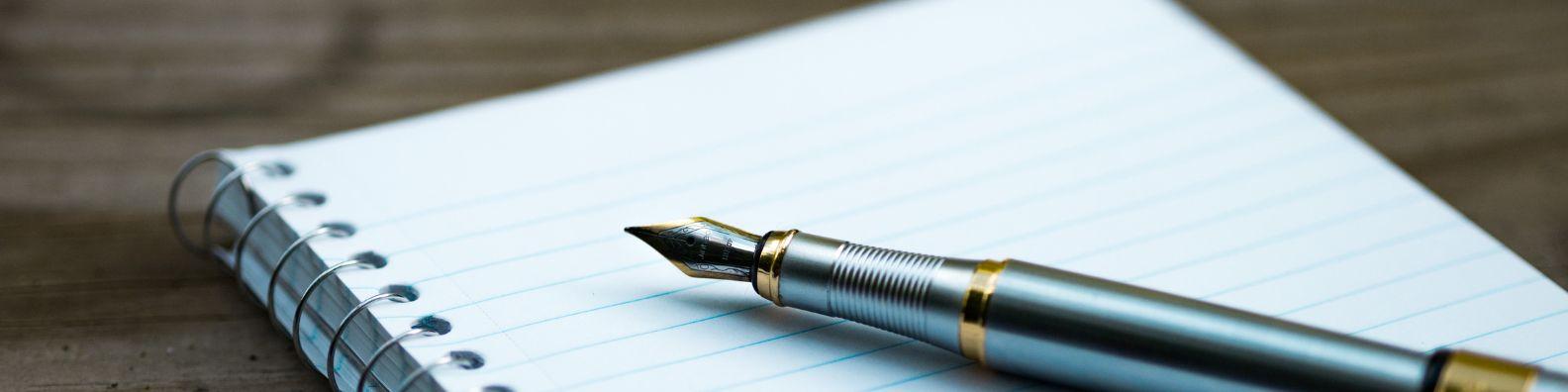 A metallic fountain pen rests on a ring bound notebook.
